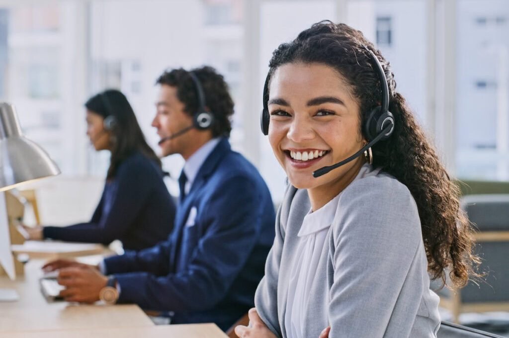Call center woman, smile and portrait at headphones, job and staff group with computer, advice and office. Telemarketing agent, pc and microphone at help desk, consulting or listen for tech support
